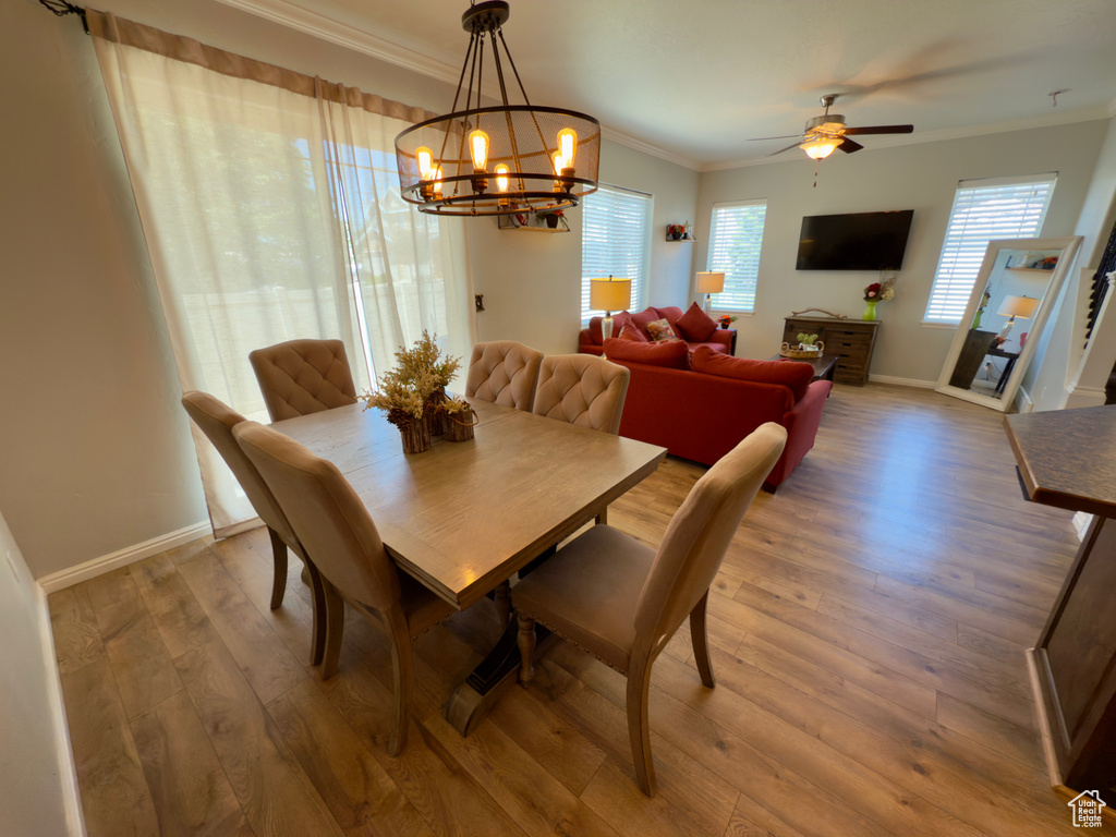 Dining area with ornamental molding, a chandelier, wood finished floors, a ceiling fan, and baseboards