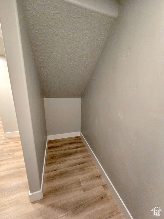 Interior space featuring wood finished floors, baseboards, a textured ceiling, and lofted ceiling