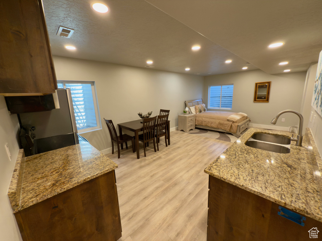 Kitchen featuring a sink, light wood-style flooring, recessed lighting, light stone counters, and baseboards