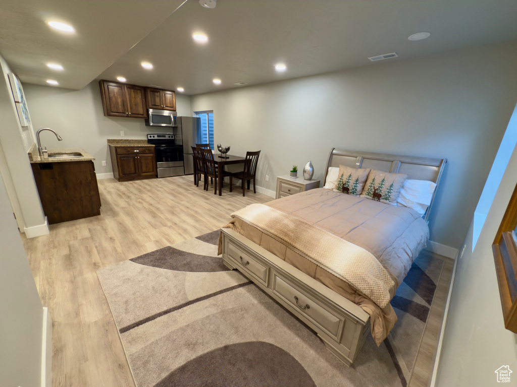 Bedroom with light wood-type flooring, recessed lighting, and bar with sink