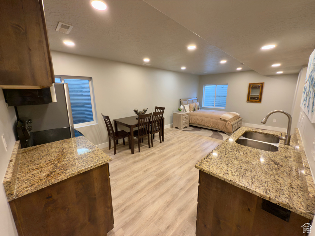 Kitchen with light wood-type flooring, recessed lighting, light stone counters, dark brown cabinetry, and stove