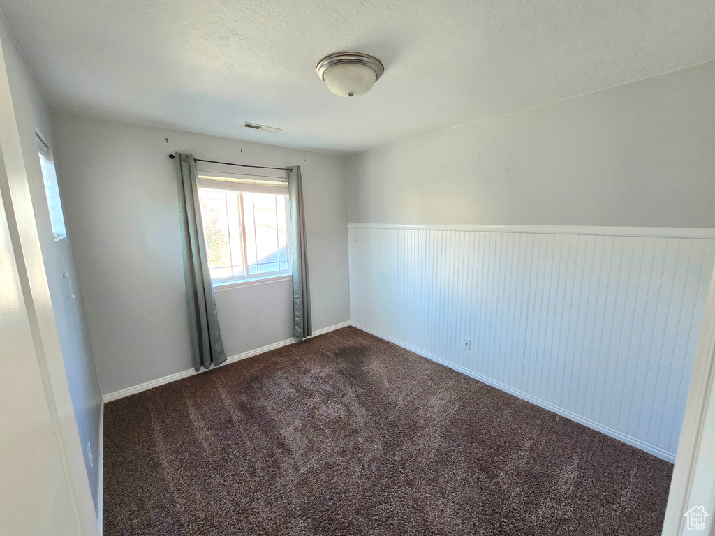 Carpeted empty room with a wainscoted wall and a textured ceiling