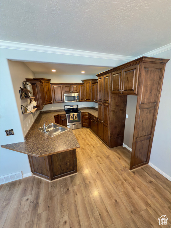 Kitchen with appliances with stainless steel finishes, a peninsula, a sink, crown molding, and dark countertops