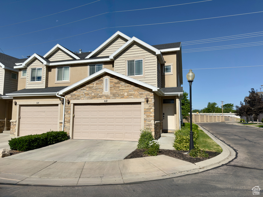 View of property with stone siding, driveway, a garage, and stucco siding
