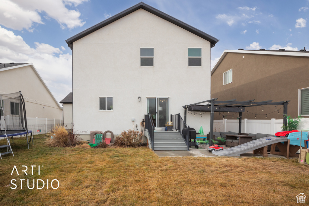 Back of house featuring a trampoline, stucco siding, a pergola, and a patio area