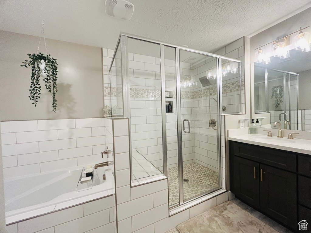 Bathroom featuring vanity, a stall shower, a bath, and a textured ceiling