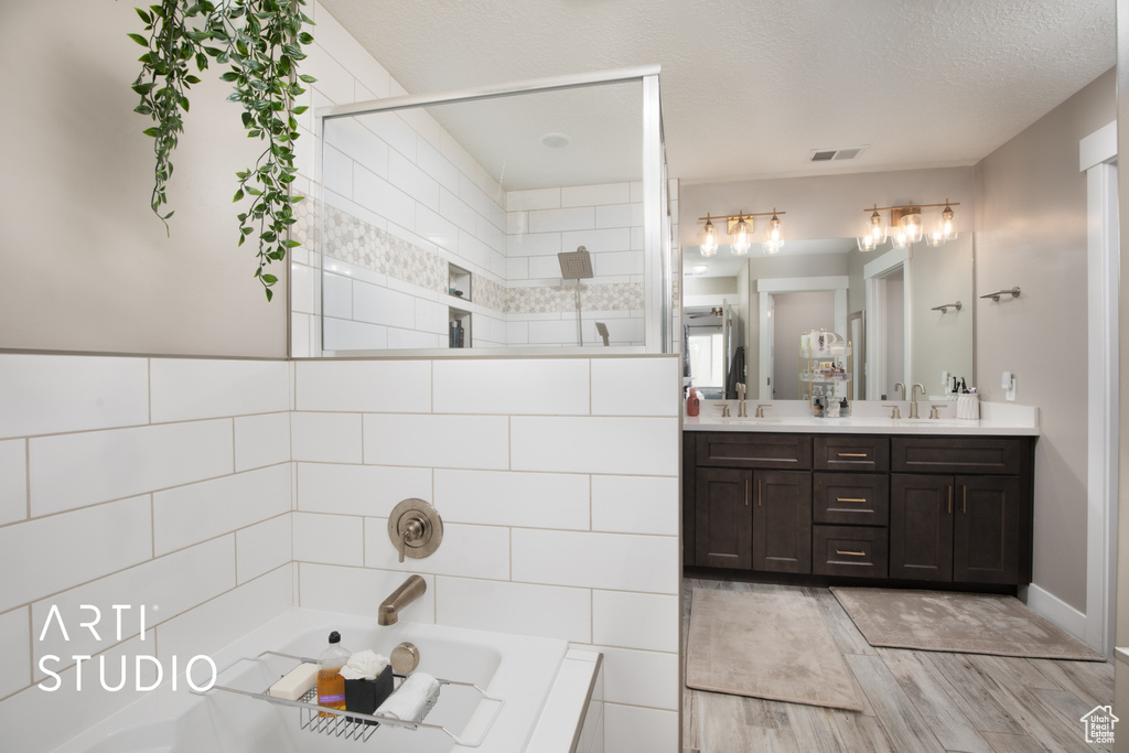 Bathroom with double vanity, a bath, wood finished floors, and a tile shower