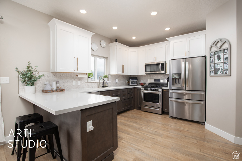Kitchen featuring appliances with stainless steel finishes, a peninsula, white cabinets, a kitchen bar, and recessed lighting