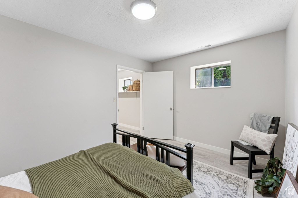 Bedroom with light wood finished floors, a textured ceiling, and baseboards