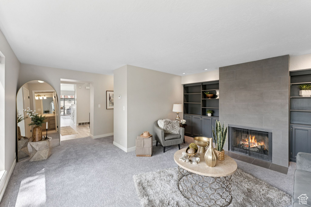 Carpeted living room with a tiled fireplace, baseboards, and arched walkways