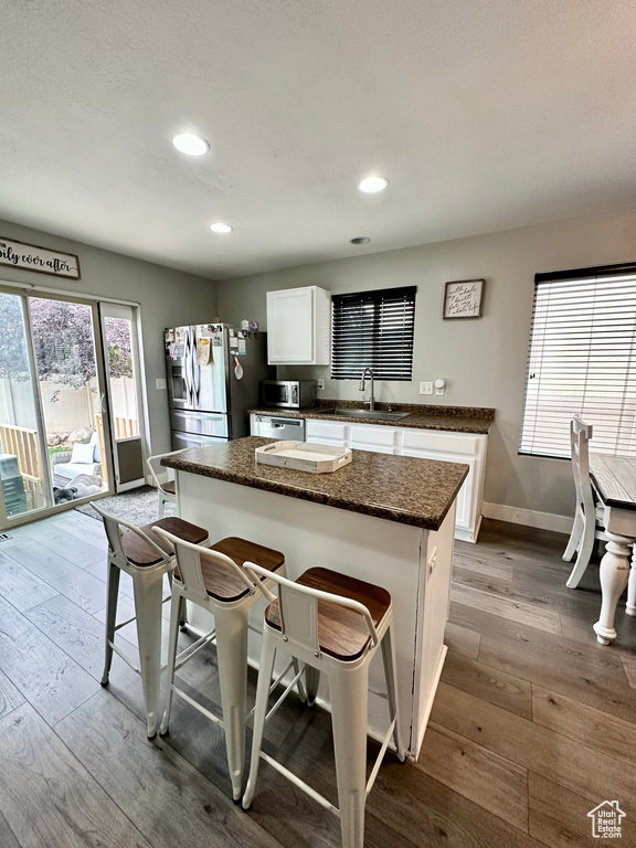 Kitchen with appliances with stainless steel finishes, a sink, a kitchen breakfast bar, dark wood-type flooring, and white cabinets