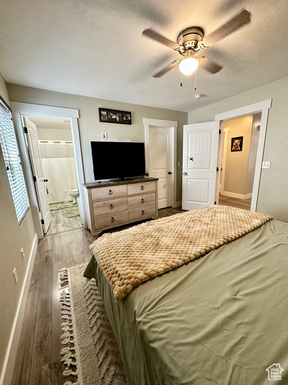 Bedroom featuring wood finished floors, baseboards, a textured ceiling, ensuite bathroom, and a ceiling fan