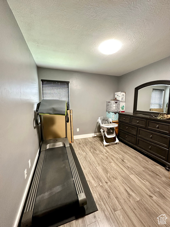 Workout room with light wood-style flooring, a textured ceiling, and baseboards
