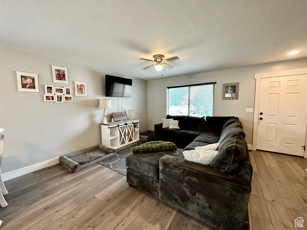 Living room with wood finished floors, a ceiling fan, baseboards, and a textured ceiling