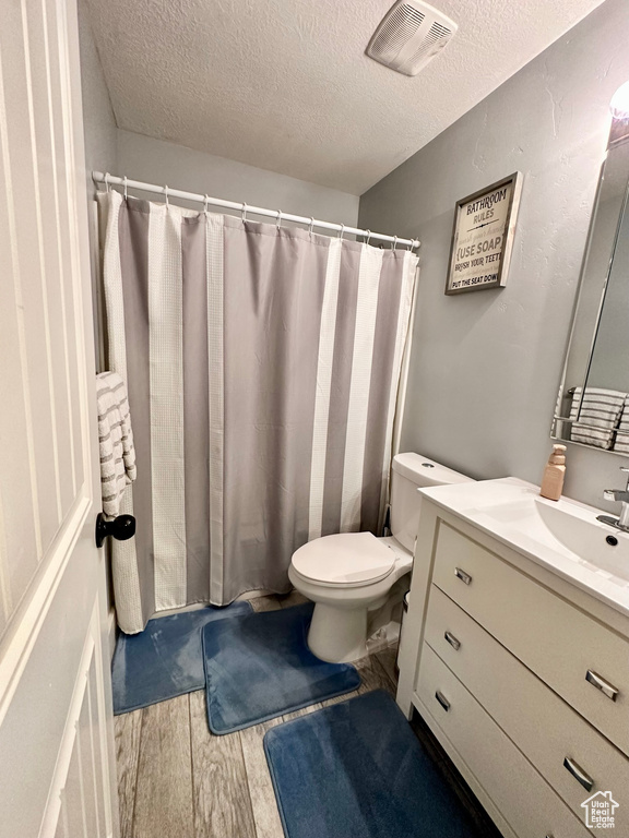 Full bathroom with a textured ceiling, wood finished floors, vanity, and toilet