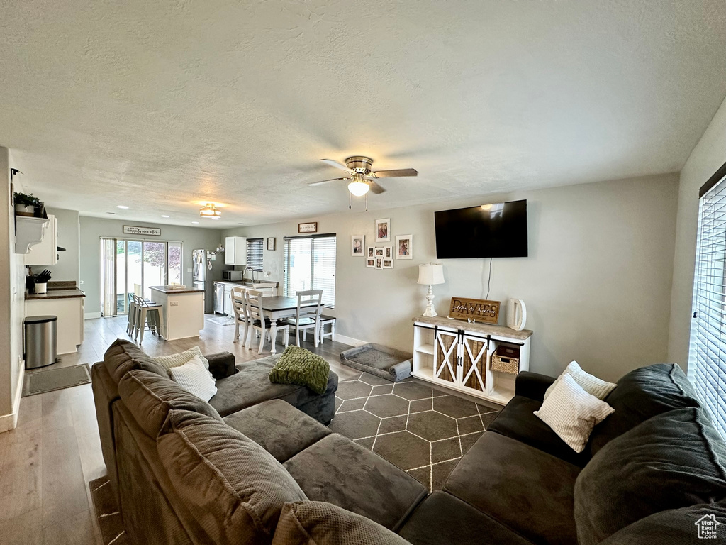 Living area with a ceiling fan, a textured ceiling, wood finished floors, and baseboards