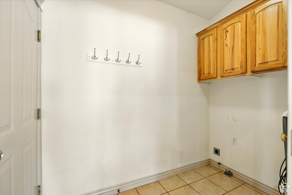 Laundry area featuring electric dryer hookup, cabinet space, light tile patterned flooring, and baseboards