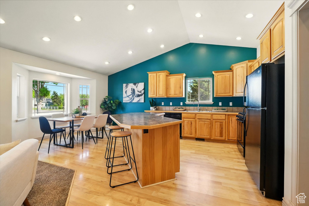 Kitchen featuring black appliances, a sink, a kitchen breakfast bar, a center island, and light wood-style flooring