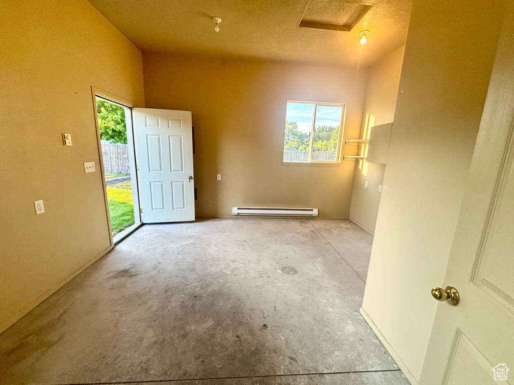 Empty room with a baseboard radiator, concrete floors, and attic access