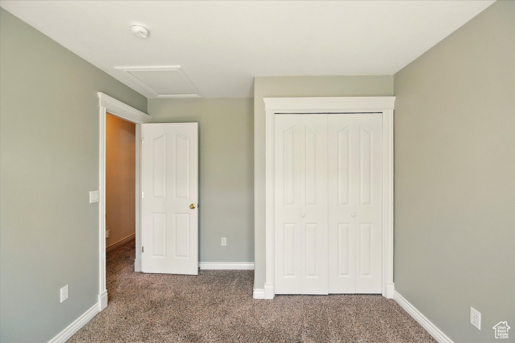 Unfurnished bedroom featuring carpet floors, attic access, baseboards, and a closet