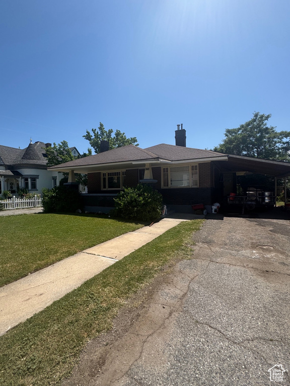 View of front of house with asphalt driveway, a carport, a front yard, and a chimney