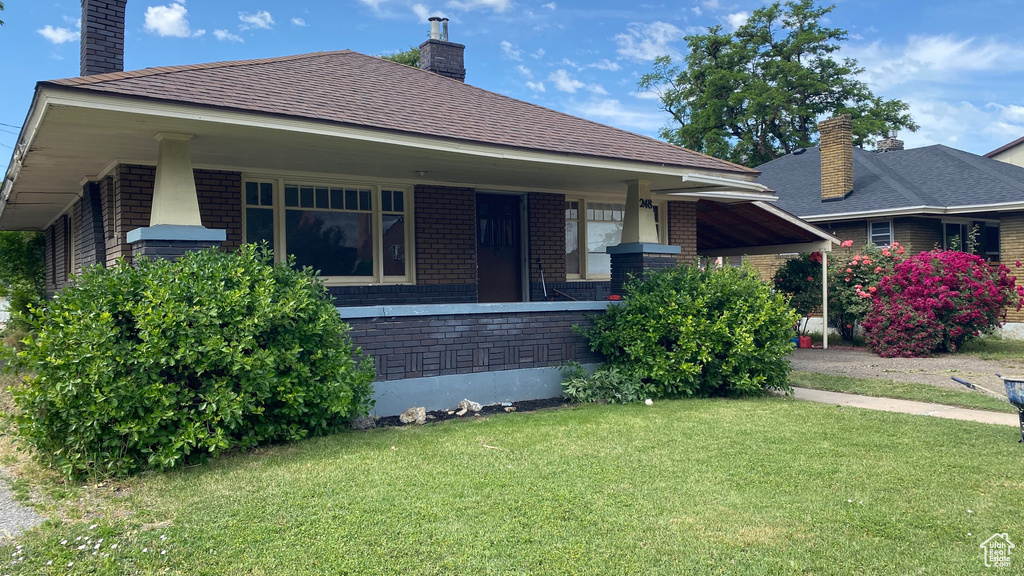 View of front of property featuring a chimney, a front yard, brick siding, and covered porch