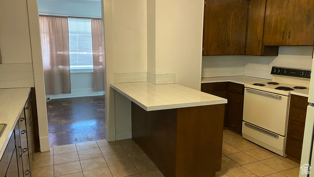 Kitchen with white range with electric stovetop, a peninsula, light countertops, and light tile patterned floors