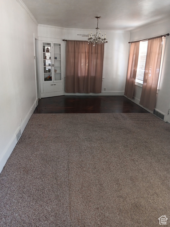 Unfurnished room featuring a chandelier, dark colored carpet, and crown molding