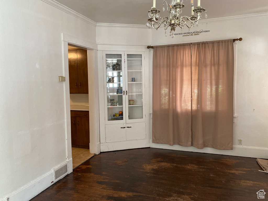 Unfurnished dining area with a chandelier, wood finished floors, crown molding, and baseboards