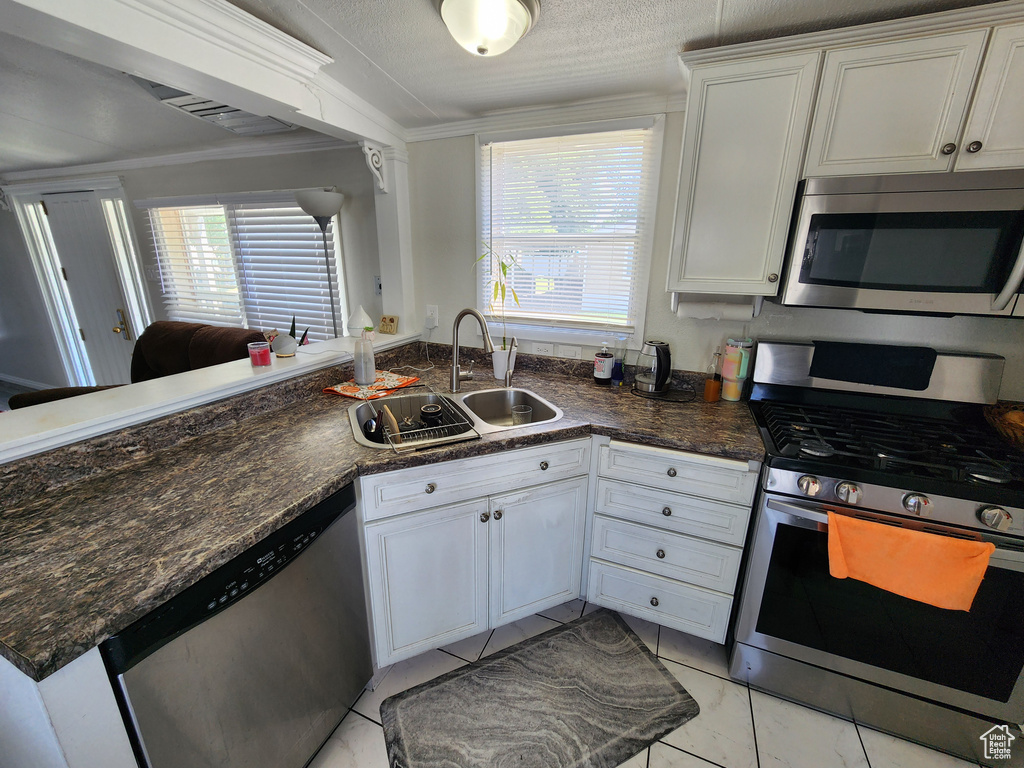 Kitchen with stainless steel appliances, a sink, plenty of natural light, white cabinetry, and crown molding