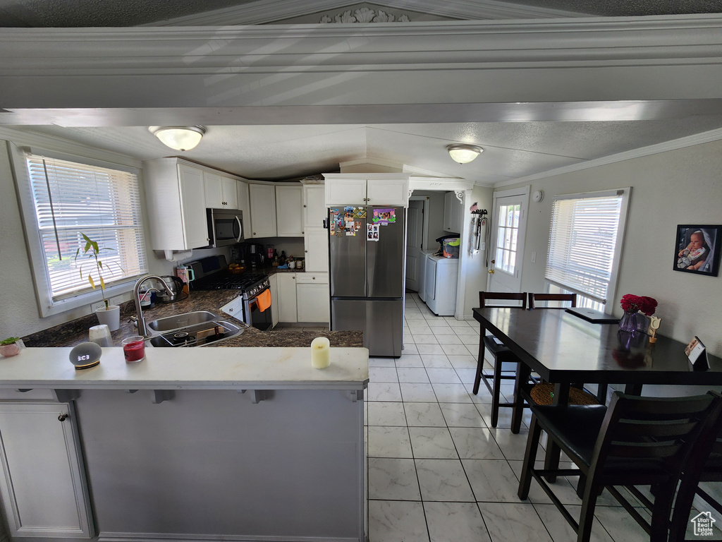 Kitchen with appliances with stainless steel finishes, a sink, washer / clothes dryer, light marble finish floors, and a peninsula