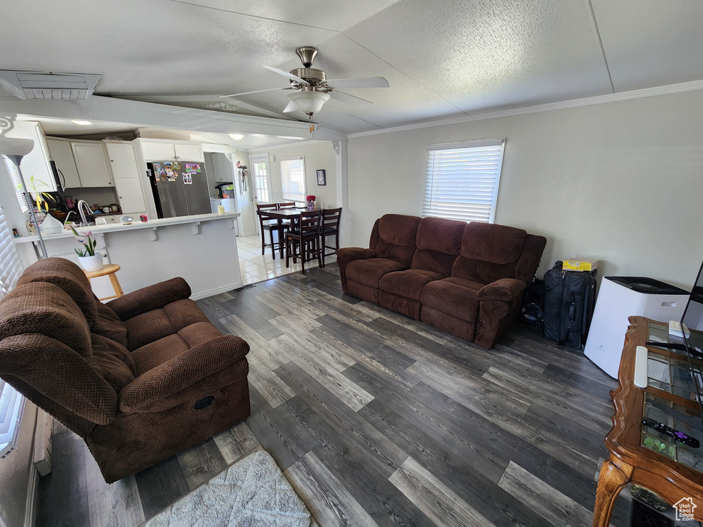 Living room with ceiling fan, dark wood-style flooring, crown molding, and vaulted ceiling
