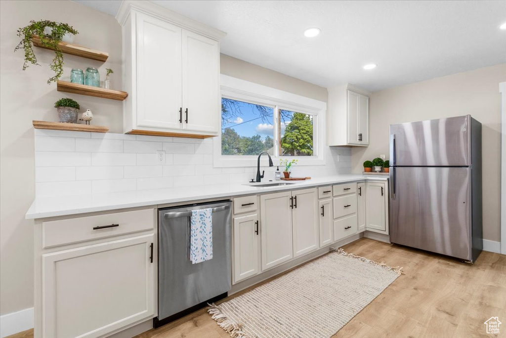 Kitchen with stainless steel appliances, a sink, tasteful backsplash, light wood-style floors, and open shelves