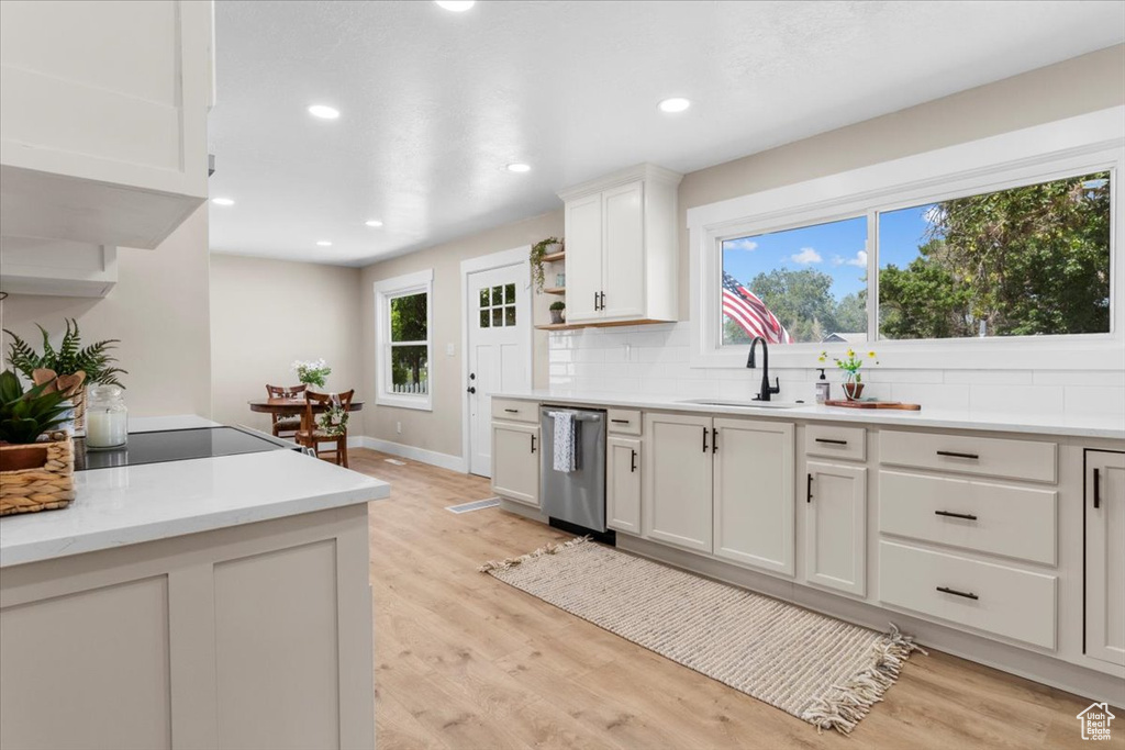 Kitchen with stainless steel dishwasher, a sink, tasteful backsplash, light countertops, and light wood-style floors