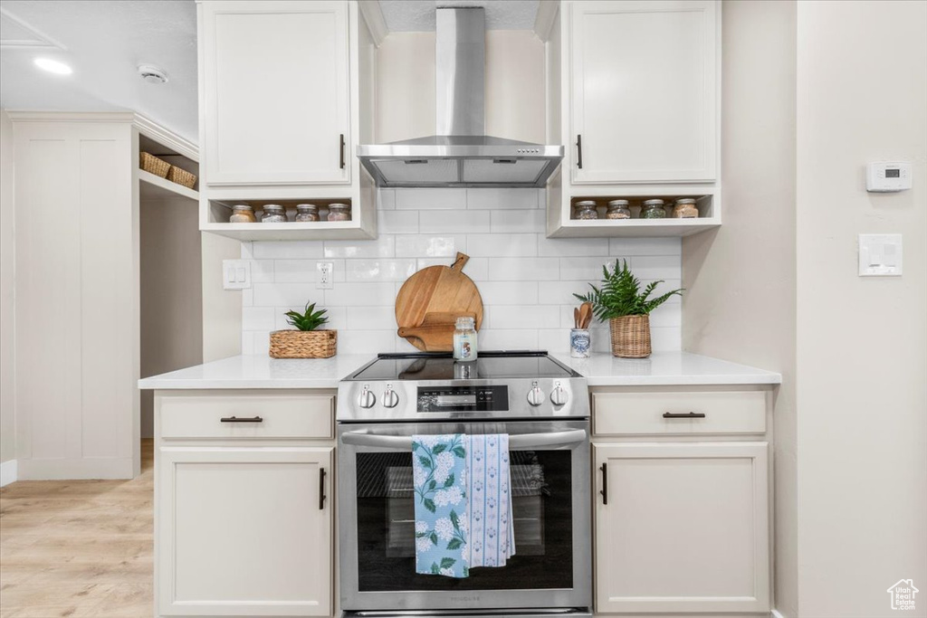 Kitchen with stainless steel electric range oven, wall chimney exhaust hood, open shelves, backsplash, and light countertops