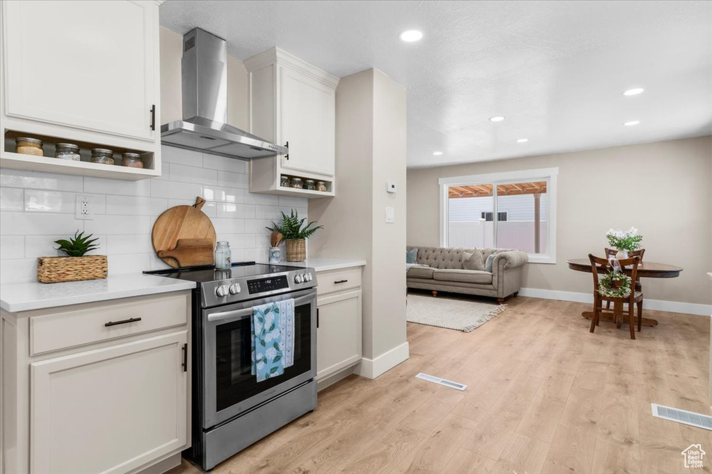 Kitchen featuring electric range, wall chimney exhaust hood, baseboards, decorative backsplash, and light countertops