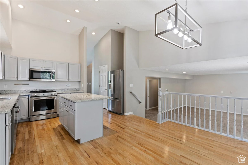 Kitchen with stainless steel appliances, high vaulted ceiling, gray cabinets, a center island, and light wood finished floors