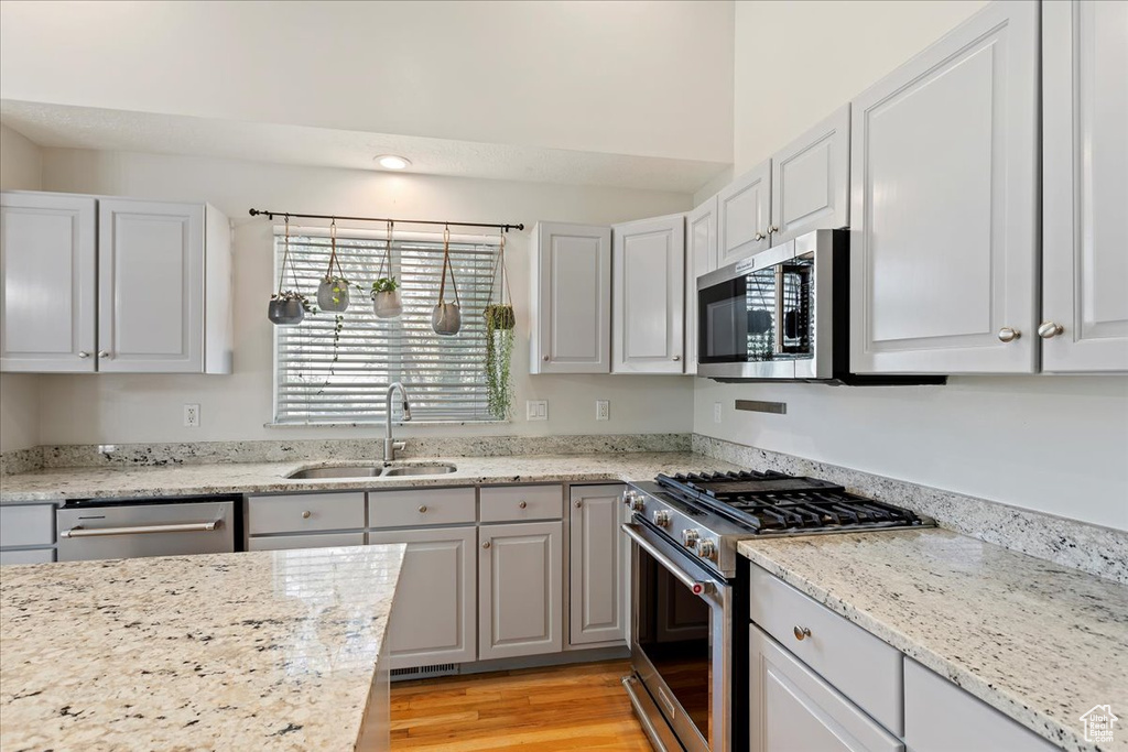 Kitchen with stainless steel appliances, a sink, light wood-type flooring, light stone counters, and recessed lighting