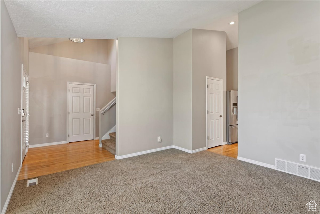 Carpeted empty room featuring baseboards, a high ceiling, stairway, recessed lighting, and a textured ceiling