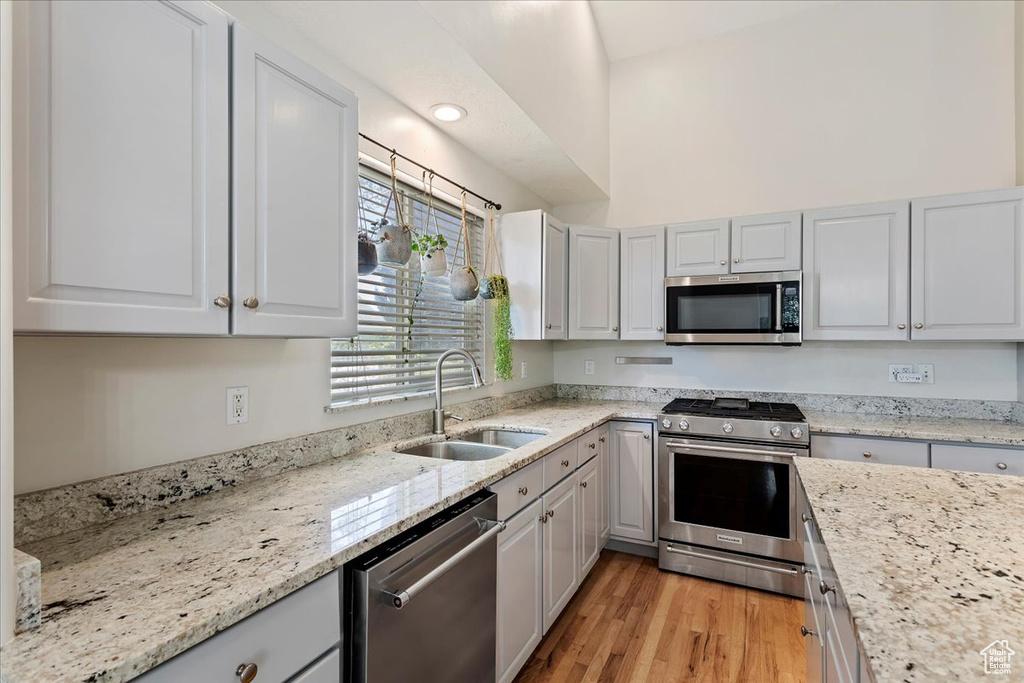 Kitchen featuring appliances with stainless steel finishes, a sink, light stone countertops, and light wood finished floors