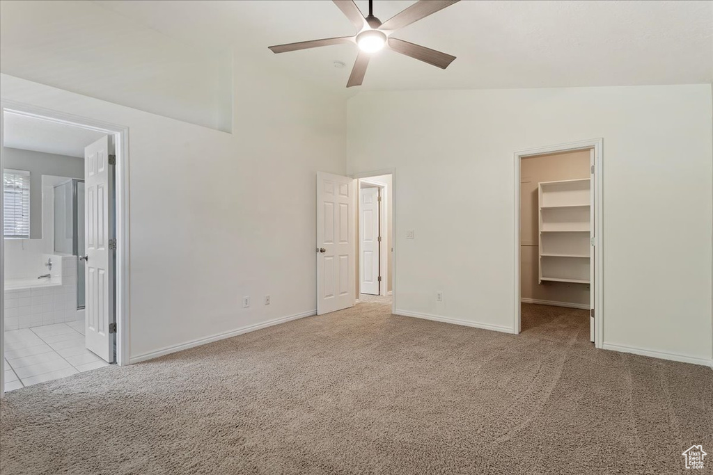 Unfurnished bedroom featuring a spacious closet, light carpet, vaulted ceiling, a closet, and baseboards