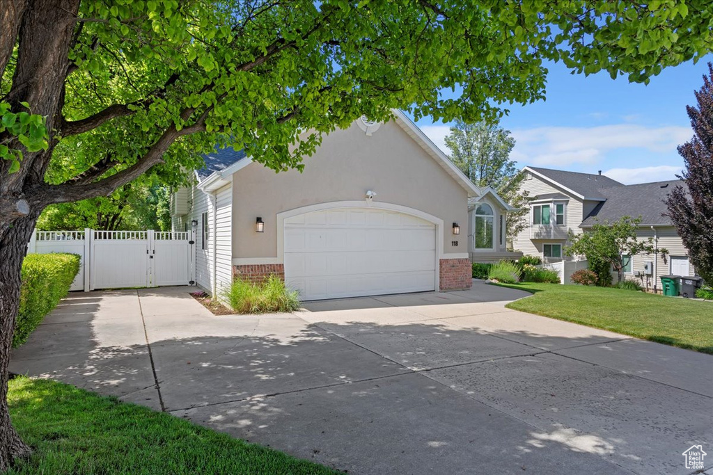 View of front facade featuring brick siding, a gate, driveway, an attached garage, and stucco siding