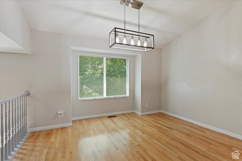 Unfurnished dining area featuring wood finished floors, baseboards, and a chandelier