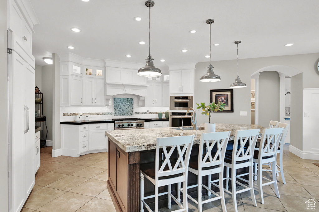 Kitchen with arched walkways, light tile patterned floors, backsplash, a center island with sink, and recessed lighting