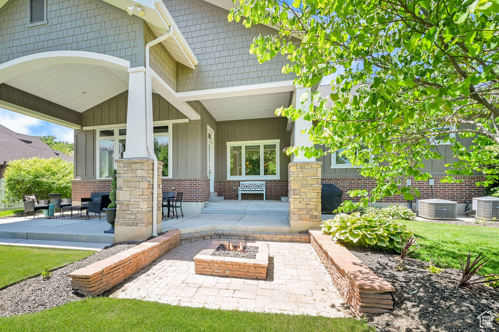Entrance to property with board and batten siding, central AC unit, brick siding, and covered porch