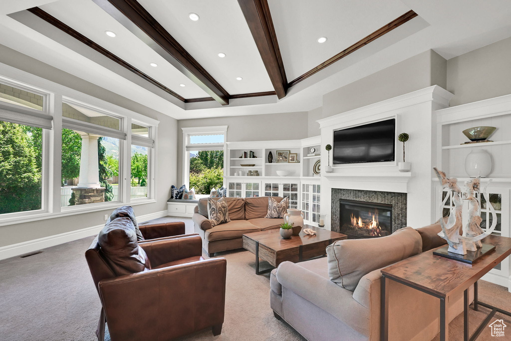 Carpeted living room with a glass covered fireplace, beam ceiling, baseboards, ornamental molding, and recessed lighting