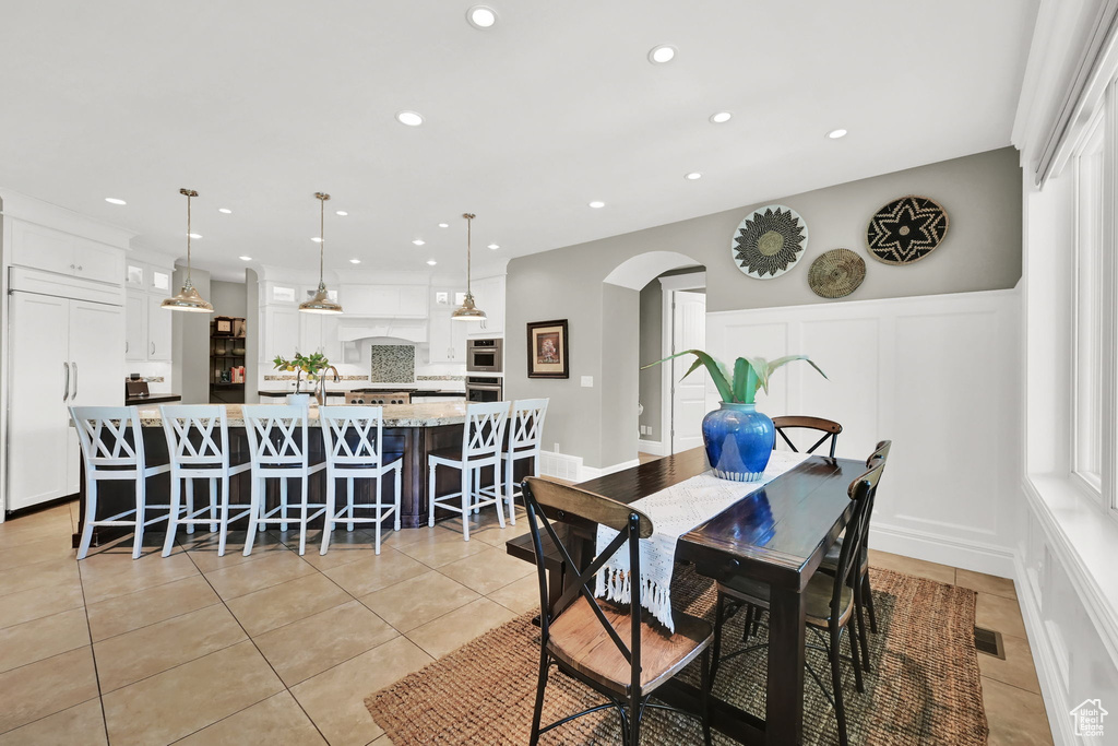 Dining area with a decorative wall, arched walkways, recessed lighting, light tile patterned floors, and wainscoting