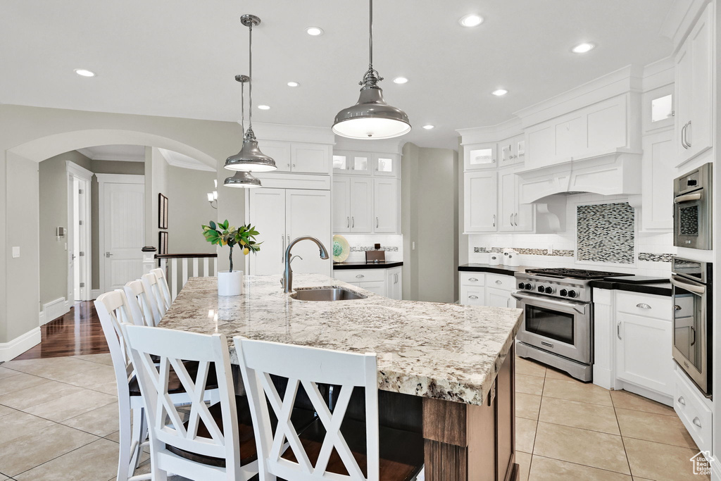 Kitchen with a sink, appliances with stainless steel finishes, light tile patterned floors, arched walkways, and recessed lighting