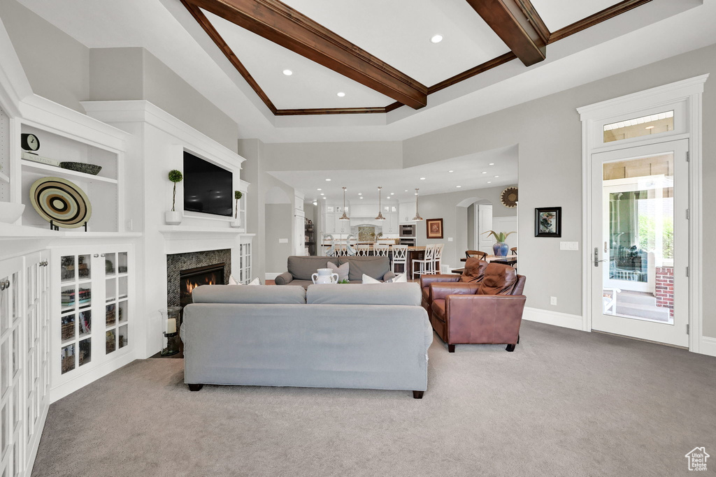 Carpeted living room with beam ceiling, a premium fireplace, recessed lighting, built in shelves, and ornamental molding