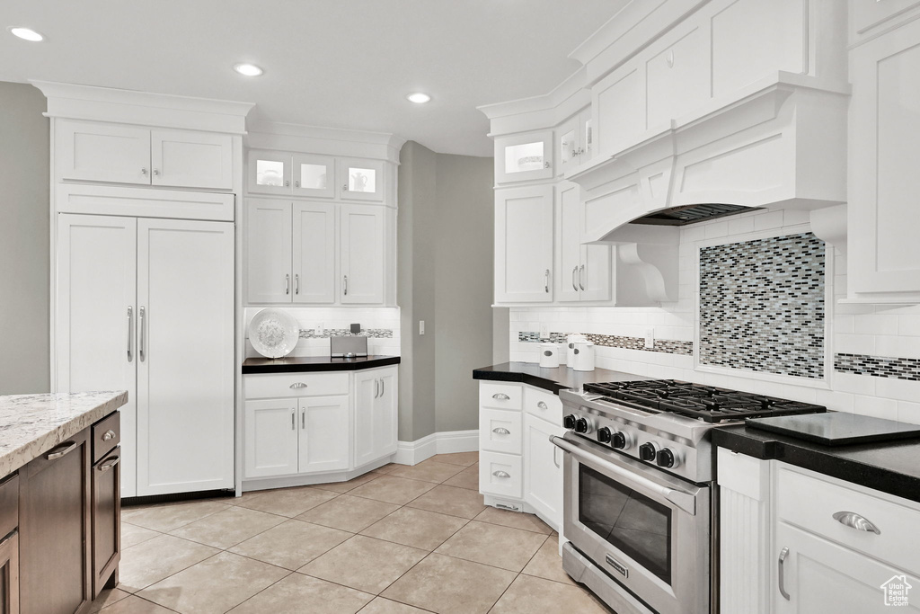 Kitchen with high quality appliances, white cabinetry, decorative backsplash, light tile patterned flooring, and glass insert cabinets